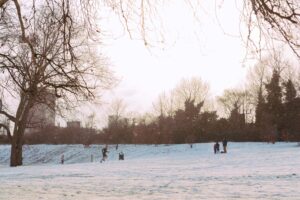 Man running across large open green space in North London which is covered in snow. 